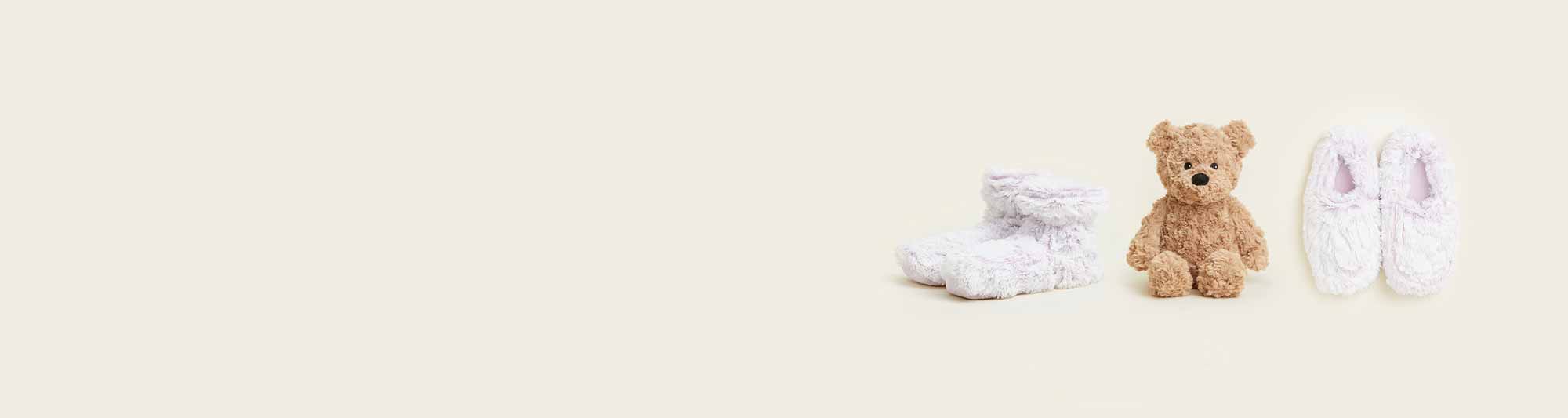 Lavender Boots Warmies, Brown Curly Bear Warmies, and Lavender Slippers lined up in a row