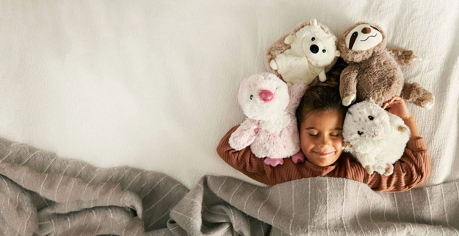 girl cuddling with pink penguin, hedgehog, sloth, and mouse stuffed animal warmies