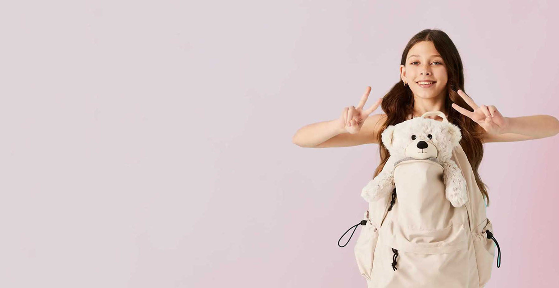 girl giving peace sign holding warmies teddy bear stuffed animal in her backpack