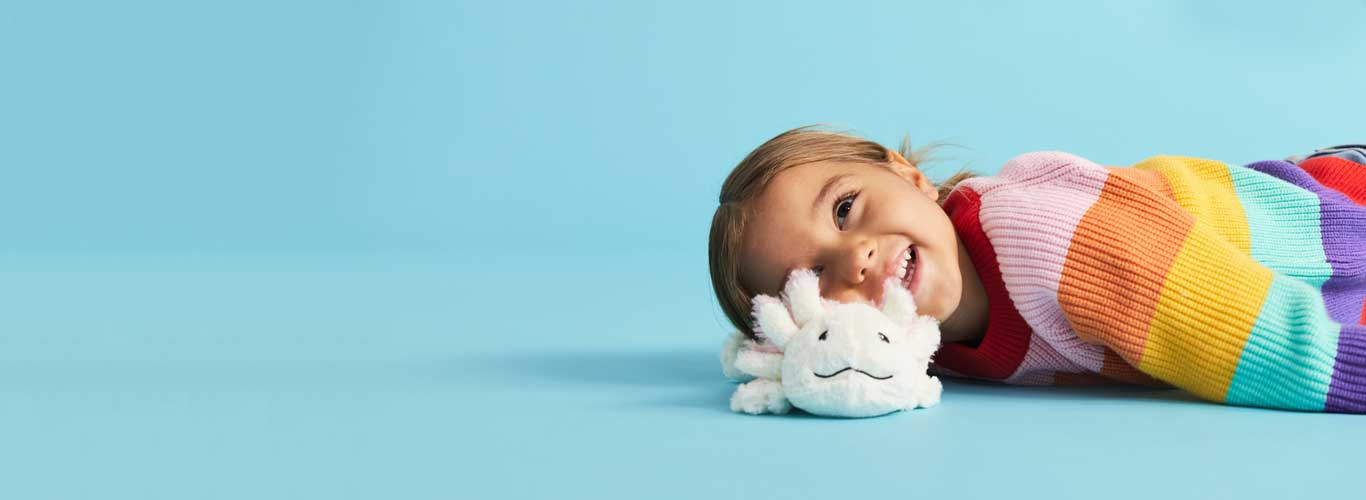Child laying down smiling with an Axolotl Warmies.