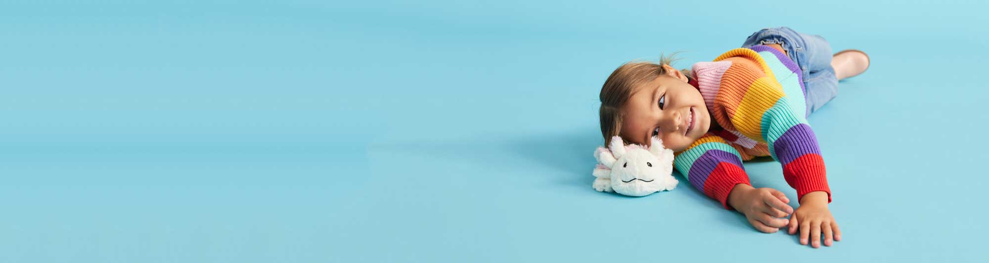 Child laying down smiling at an Axolotl Warmies.