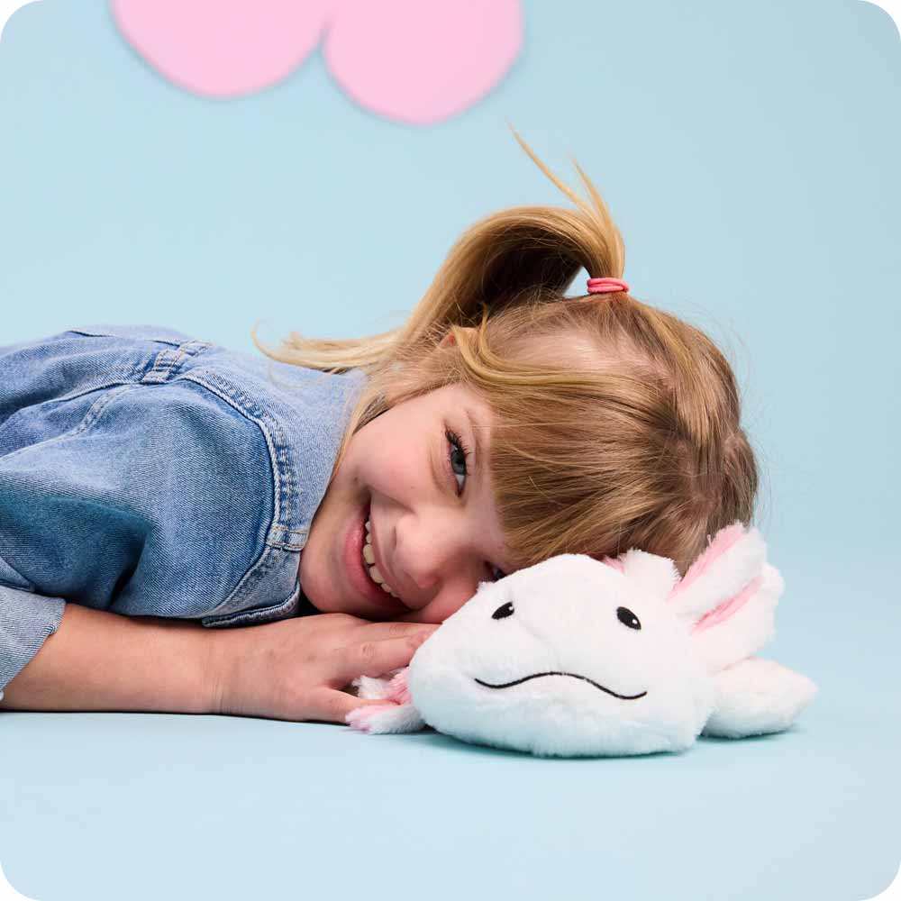 Little girl in a jean jacket laying her head on a Axolotl Warmies