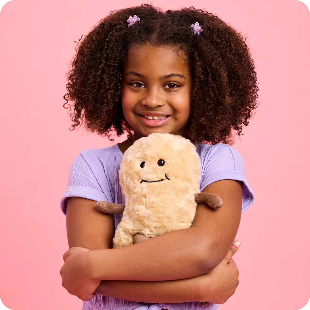 Peanut Warmies hugged by a little girl in a purple shirt against a pink backdrop.