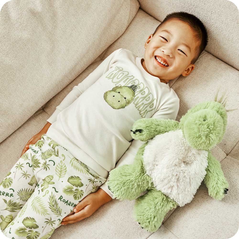 Child smiling with a Warmies Stuffed Animal while wearing Dinosaur Pajamas - Warmies USA