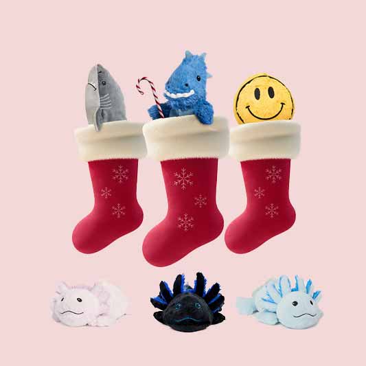 Shark, dino, smile, and colorful axolotly warmies sitting in stockings against a soft pink background