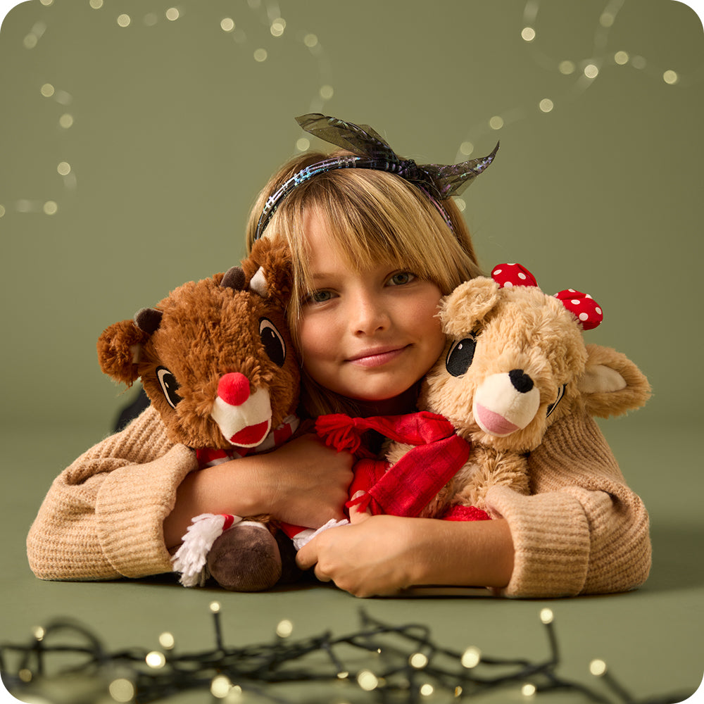 Child holding two stuffed reindeer toys with a festive background