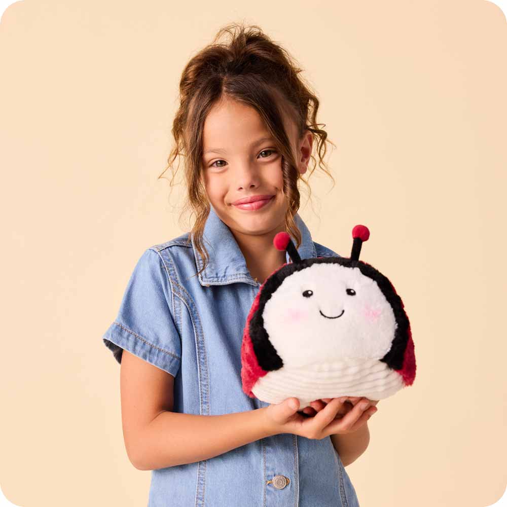 Ladybug Warmies being held by a little girl in a blue dress against a yellow background
