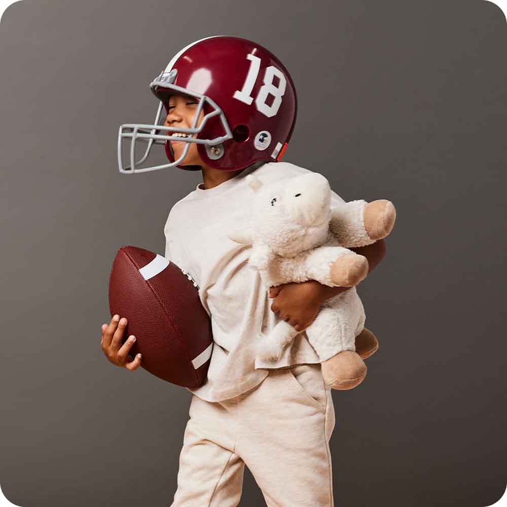 Little boy in football gear holding Soft Warm Weighted Buffalo Plush Warmies