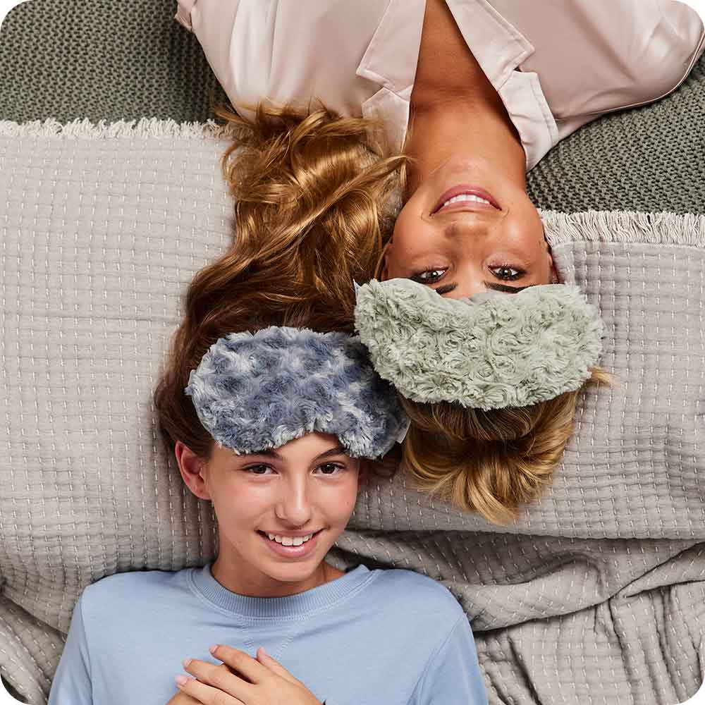 Mother and daughter smiling while wearing Microwavable Curly Gray Warmies Eye Mask
