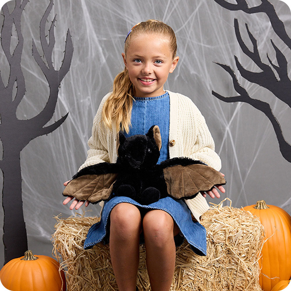 girl holding a bat stuffed animal on her lap in a halloween setting