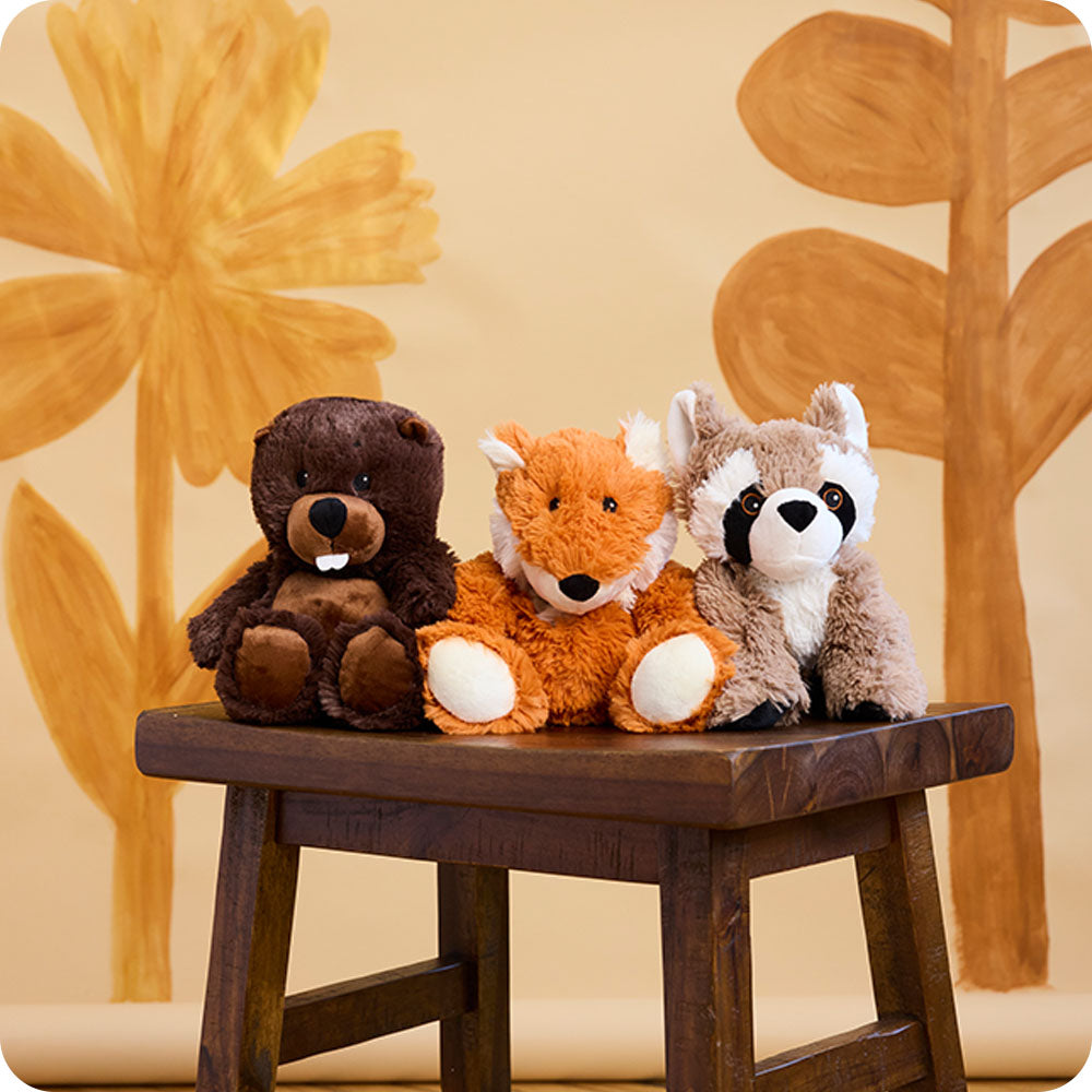 beaver, fox, and raccoon stuffed animal warmies on a bench