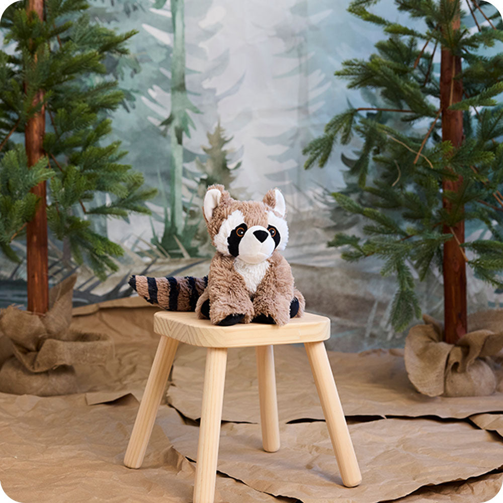 raccoon stuffed animal sitting on a stool in woodland setting