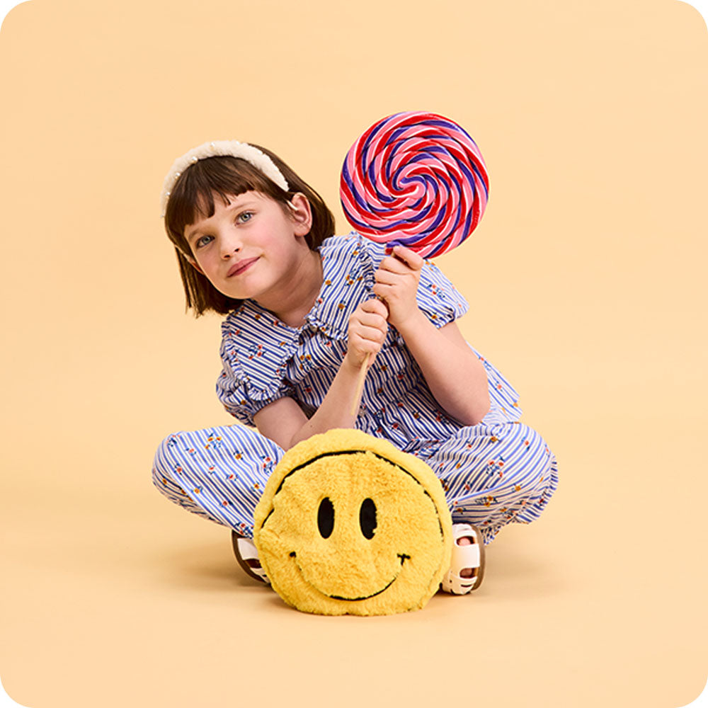 girl holding lollipop with smiley face stuffed animal warmies
