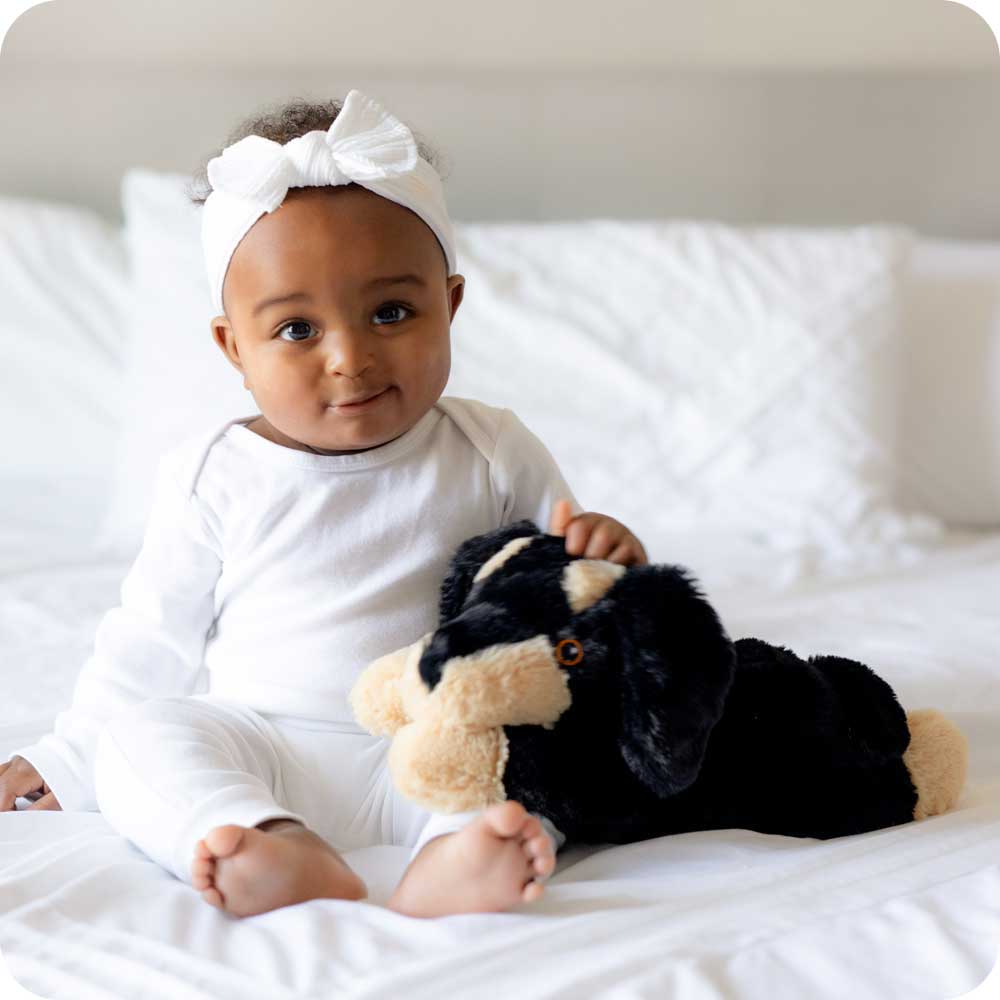 Baby girl holding Soft Warm Weighted Dachshund Plush Warmies