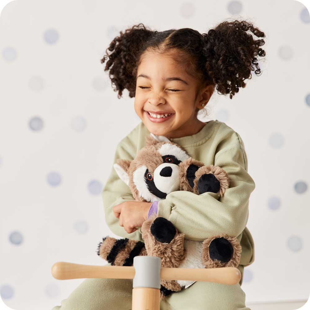 Little girl smiling and holding Cute Weighted Lavender Scented Raccoon Stuffed Animal Heating Pad Warmies