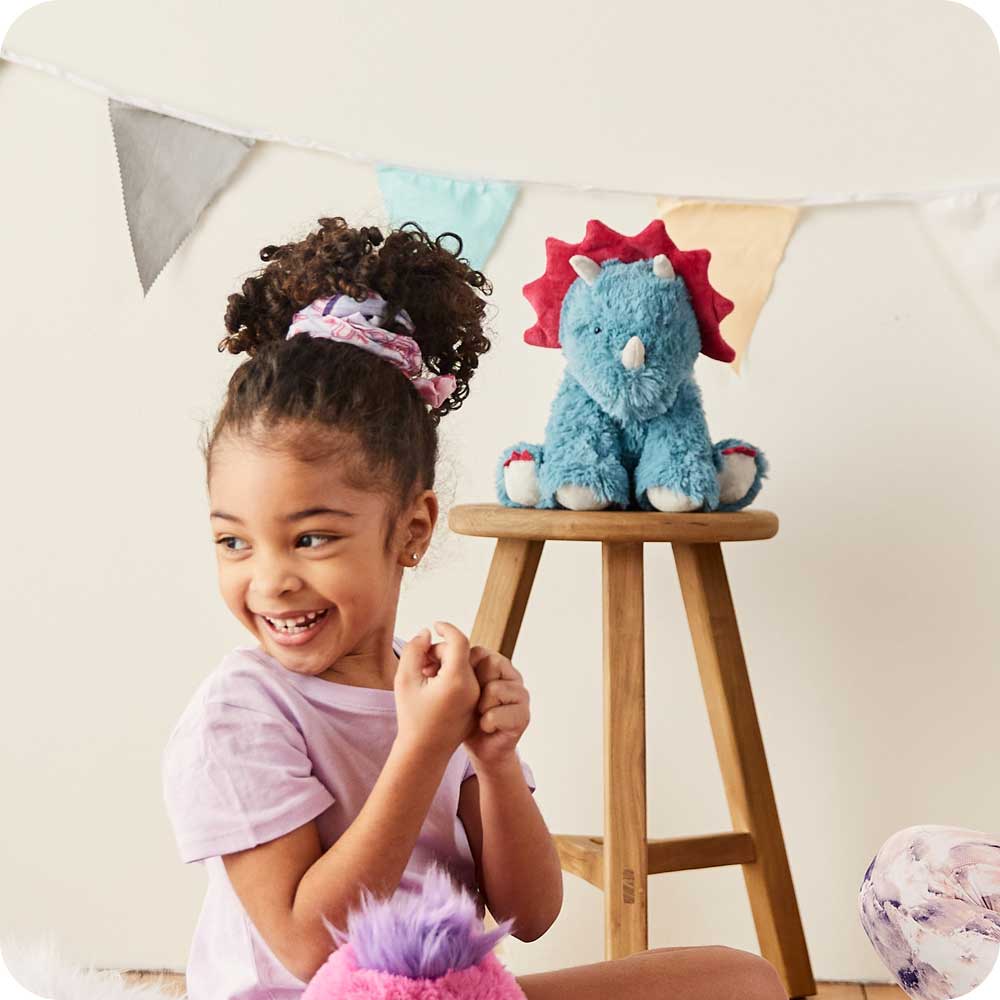 Child sitting with Cute Weighted Lavender Scented Triceratops Stuffed Animal Heating Pad Warmies