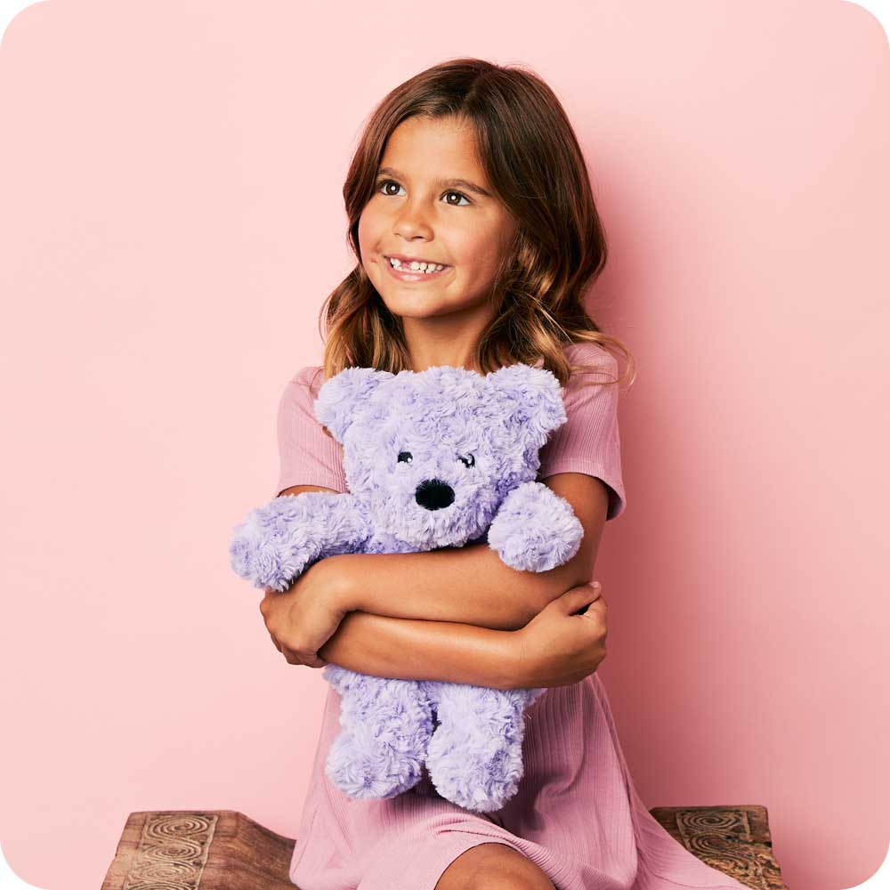 Girl smiling and hugging a Cute Weighted Lavender Scented Purple Curly Bear Stuffed Animal Heating Pad Warmies