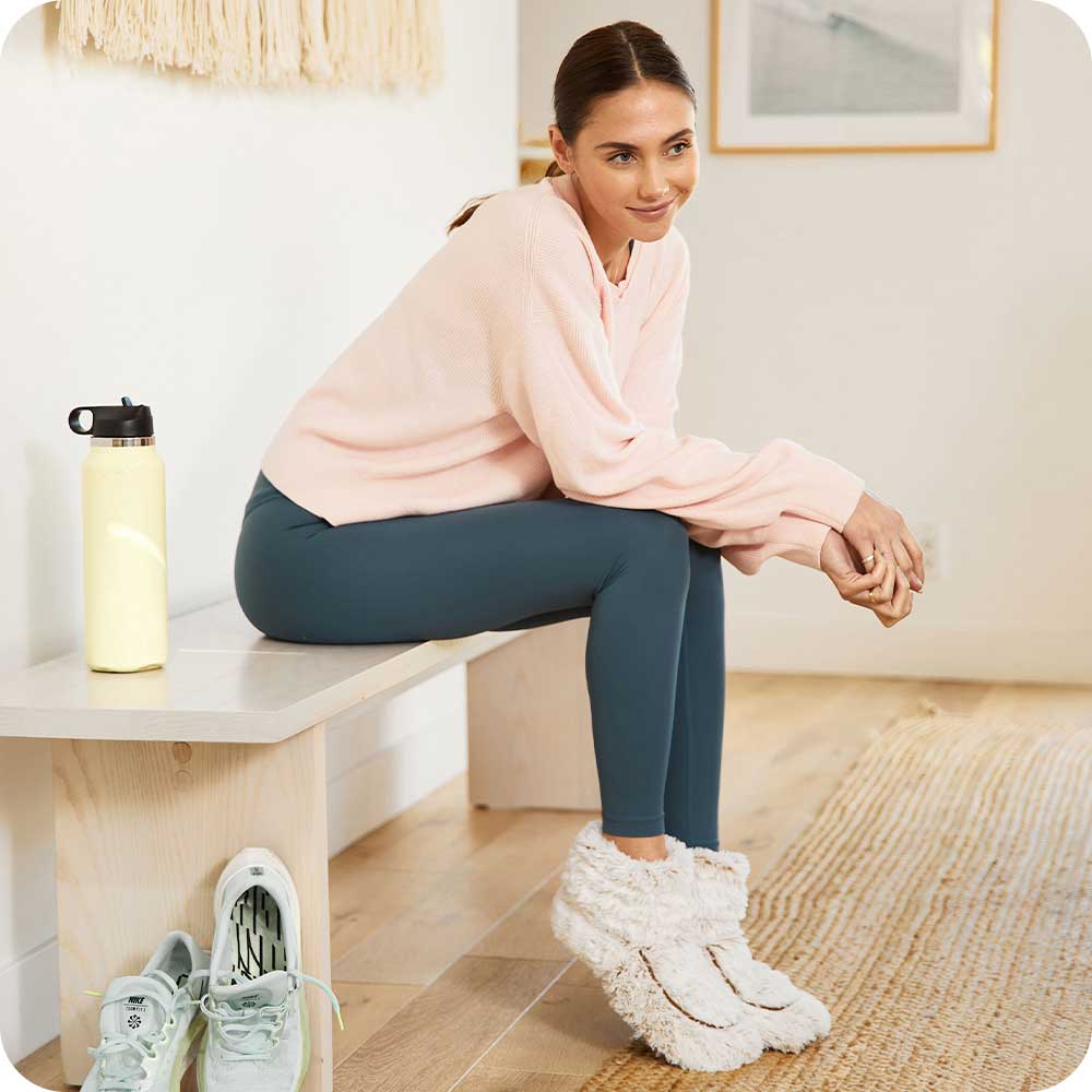 Woman sitting down and wearing Cozy Microwavable Brown Warmies Boots.