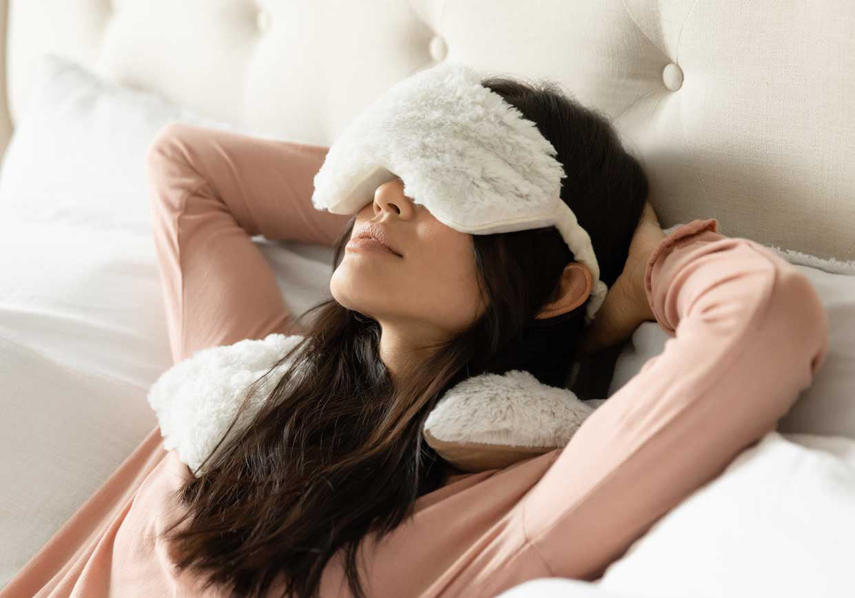 A woman resting with a Cream Eye Mask and Neck Wrap Warmies.