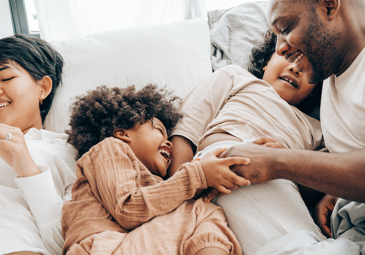 A family snuggling on a white bed.
