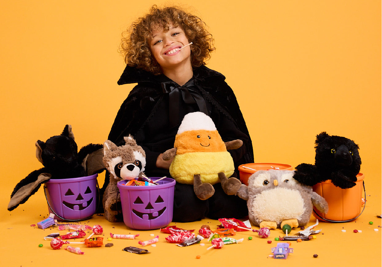 Child surrounded by candy and Raccoon, Bat, Candy Corn, Owl and Black Cat Warmies
