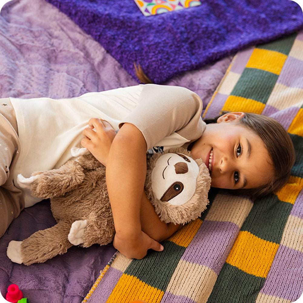 Girl with a Sloth Warmies on a blanket.