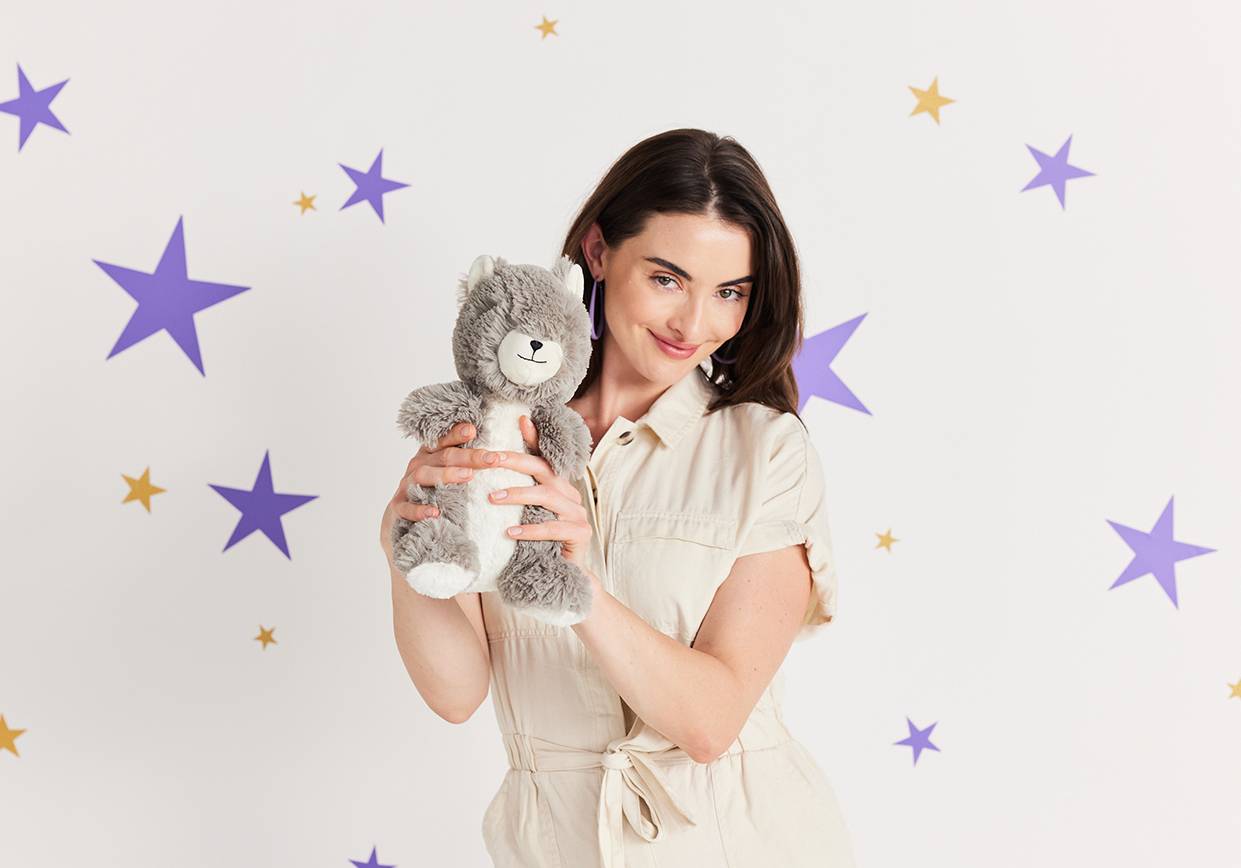 Young woman holding Warmies stuffed animal for comfort. 