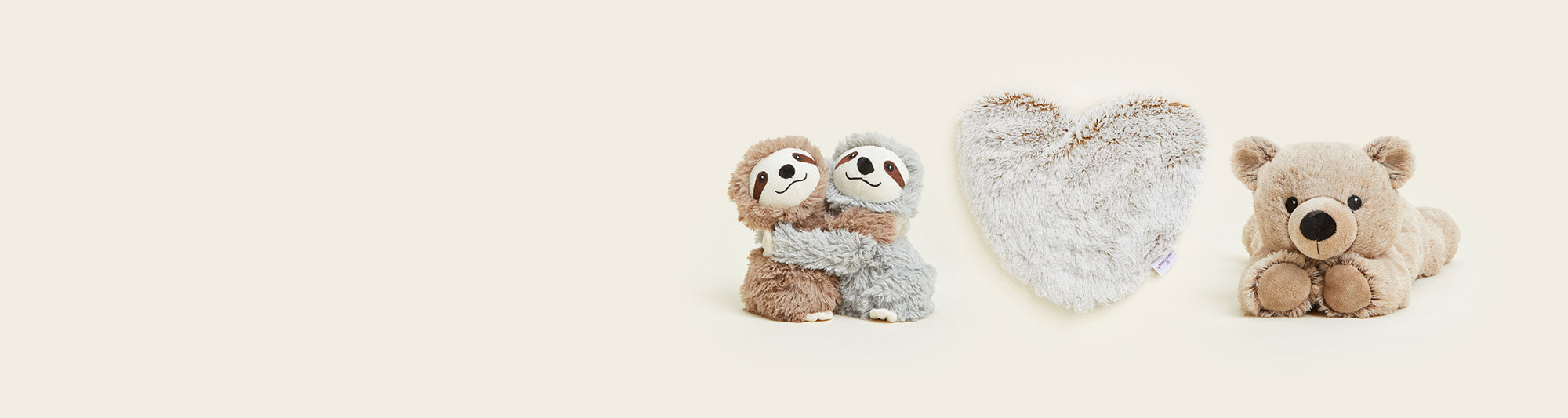 Warmies Sloth Hugs, Marshmallow Heart Heat Pad, and Brown Laying Down Bear Warmies lined up in a row