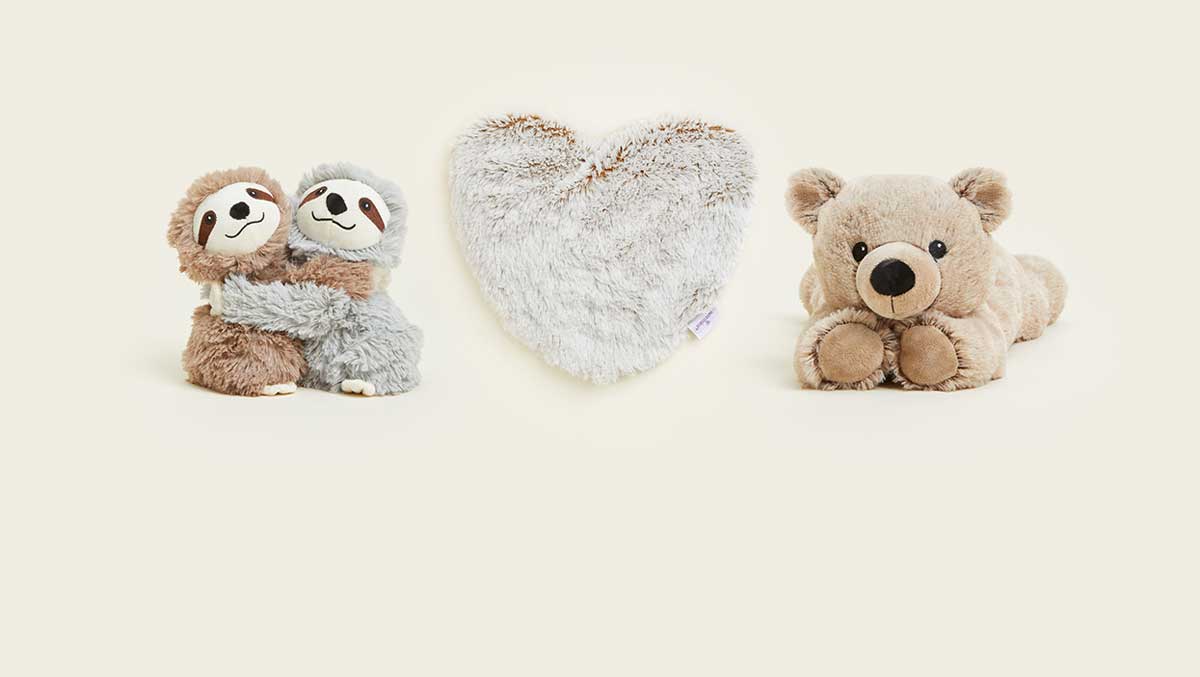 Warmies Sloth Hugs, Marshmallow Heart Heat Pad, and Brown Laying Down Bear Warmies lined up in a row