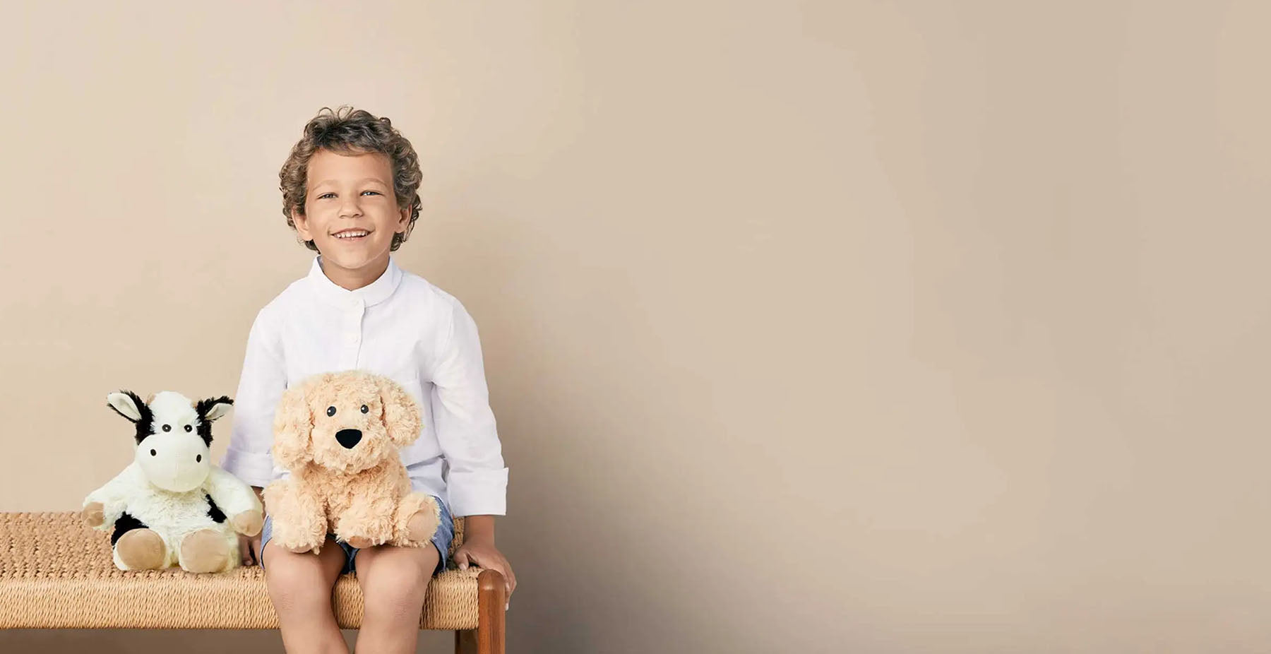 boy with cow and dog stuffed animal warmies sitting on bench