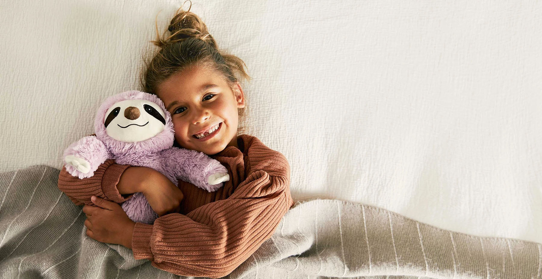 girl cuddling pink sloth stuffed animal warmies