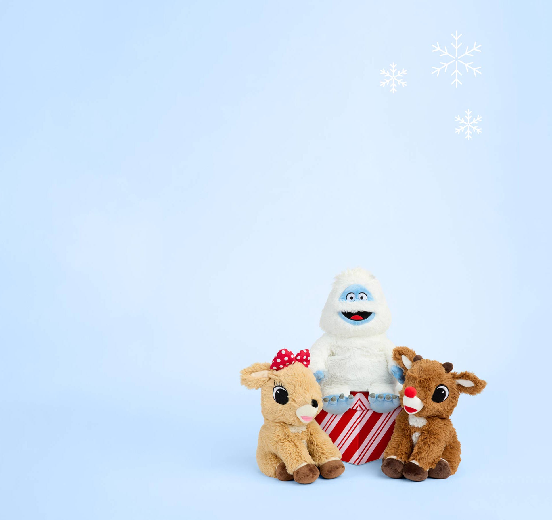 Clarice Warmies, Bumble Warmies and Rudolph Warmies sitting around a present wrapped in red and white paper