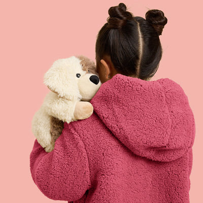 Child in a pink hoodie hugging Puppy Warmies