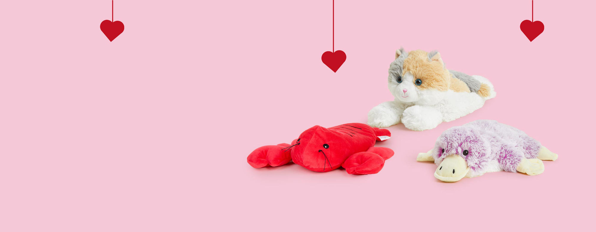 Lobster, Calico Cat, and Platypus Warmies sitting in a group with red hearts. 