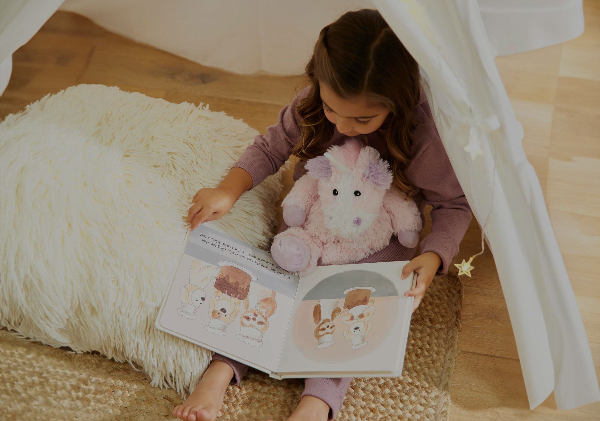 Child sitting down reading a Warmies book with Unicorn Warmies Stuffed Animal. 