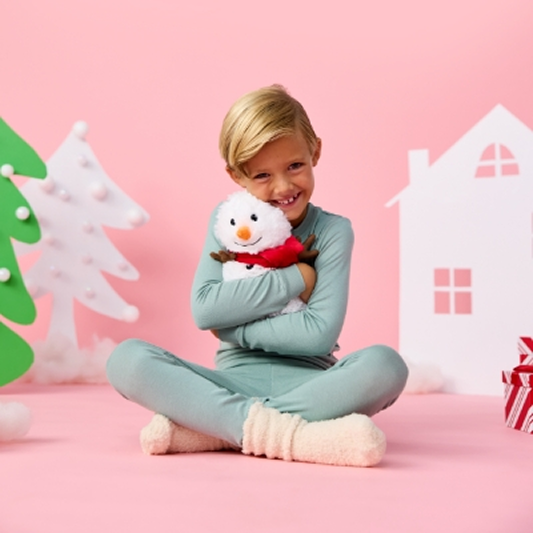 A little boy hugging a snowman warmies behind a pink christmas decorated background