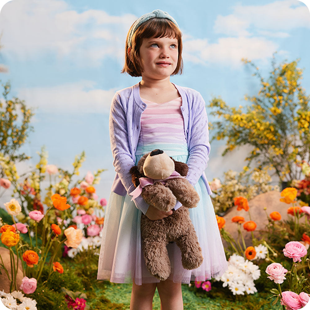 girl holding warmies dog stuffed animal in flower field