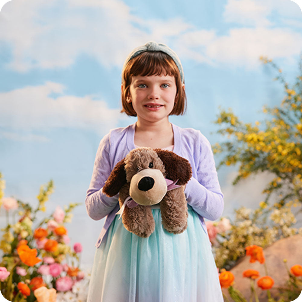 girl holding a brown dog stuffed animal in a flower field
