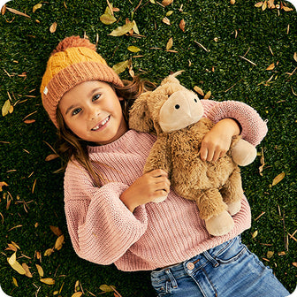girl wearing sweater holding warmies donkey stuffed animal