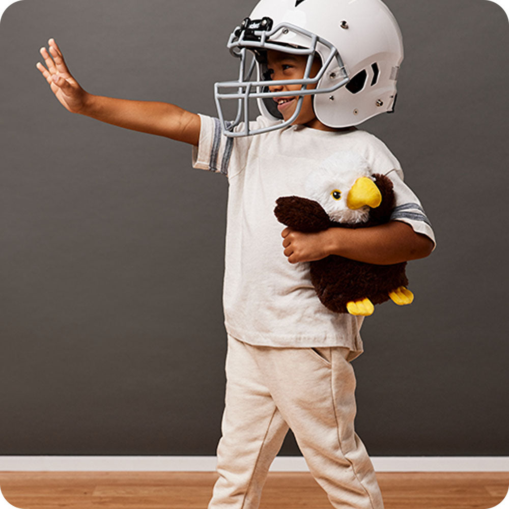 boy in football gear holding an eagle stuffed animal
