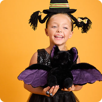 girl dressed up for halloween holding purple bat stuffed animal warmies