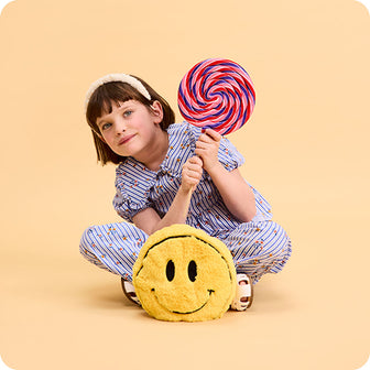 girl holding lollipop with smiley face stuffed animal warmies