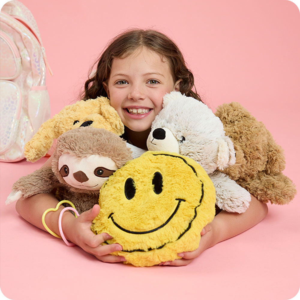 girl hugging pile of stuffed animals with smiley face stuffed animal warmies