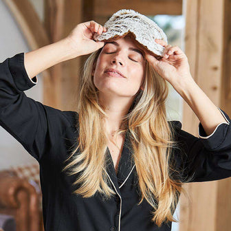 Woman relaxing while wearing Cozy Comforting Marshmallow Brown Warmies Eye Mask: Microwavable comfort for serene relaxation.